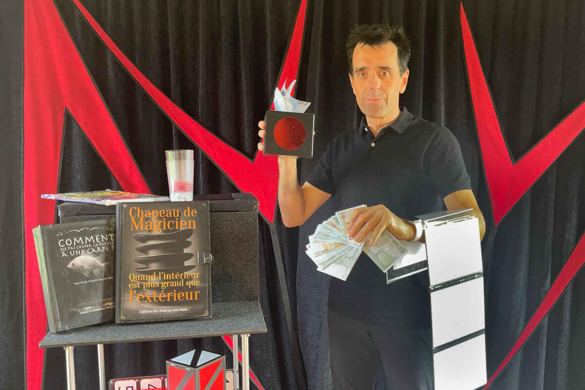 Monsieur Fred présente un livre magique et utilise une boîte pour faire apparaître des doudous sur scène, émerveillant le jeune public lors du spectacle d'une entreprise au moment des fêtes de Noël