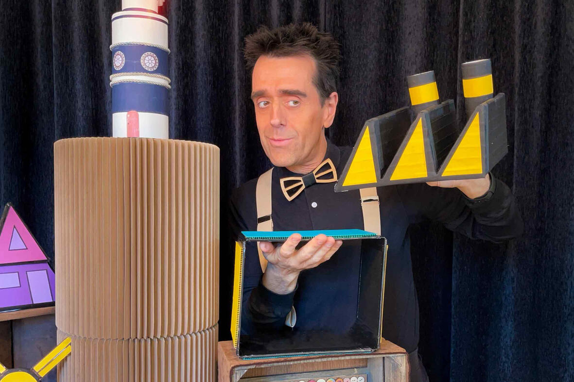 Monsieur Fred en spectacle, entouré de l’univers de Risque-Tout avec le village, la maison et l’île, offrant des surprises aux enfants en cette saison de Noël enchantée.