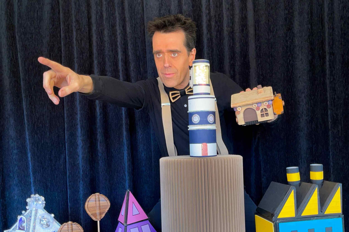 Photo du spectacle “Risque-Tout” : Monsieur Fred anime la scène avec la petite maison, l’île et le personnage principal devant un public d’enfants pour les événements jeunesse de Noël.