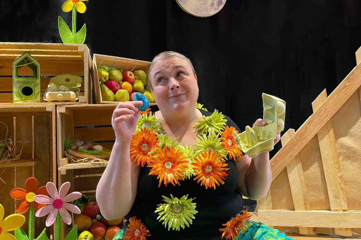 Scène de spectacle : Aurore conteuse interagit avec ses personnages et accessoires dans un décor en bois et fleurs en période de Noël et vacances scolaires.