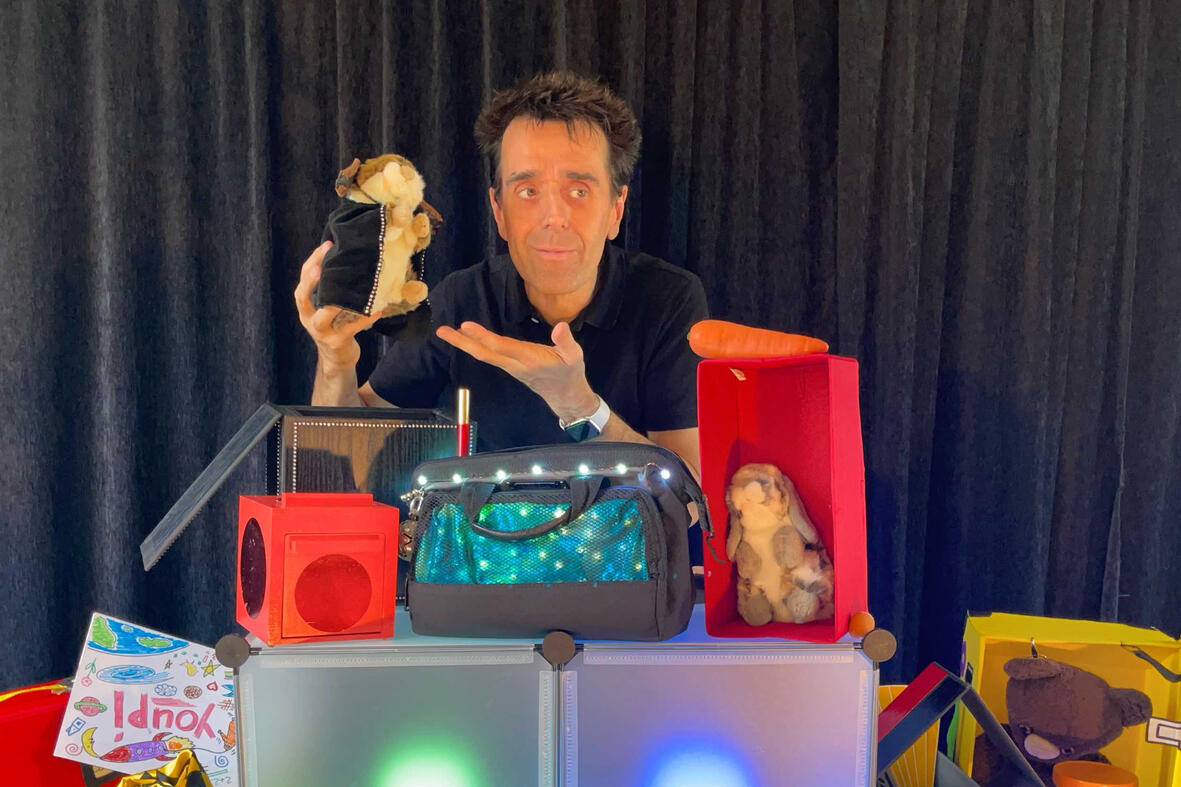 Monsieur Fred sur scène dans son décor imaginaire, présentant “Zouick, fouick, touick” à un jeune public émerveillé pour les événements de Noël.